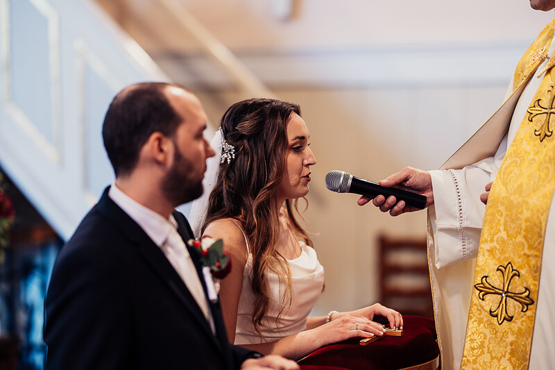 nevesta pri oltári, kňaz s mikrofónom, cirkevný obrad, ženích a nevesta, slávnostný ceremoniál, teplé svetlo v kostole. Agropenzión Hubert, Ružindol.