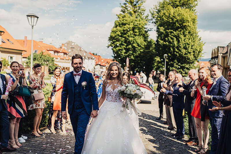nevesta s kvetmi, ženích v modrom obleku, svadobný sprievod na ulici, hostia tlieskajú, slnečný deň v mestečku, kamenná ulica s lampou. Meridiana Resort, Bojnice.