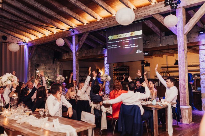 hostia so zdvihnutými rukami, tanec na svadbe, drevený strop s trámami, fialové osvetlenie, svadobný banket, papierové lampióny nad stolom. Meridiana Resort, Bojnice.