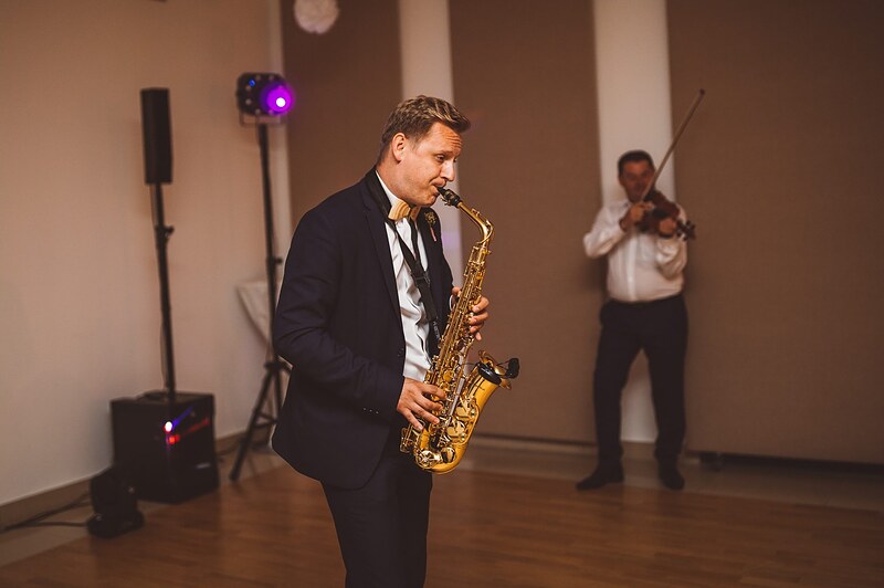 saxofonista hrá uprostred sály, husľista pri stene, reproduktory a svetlá okolo. Bašta Pajštún, Borinka.