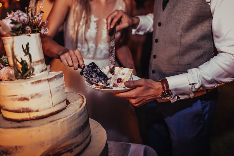 ženích a nevesta krájajú tortu, viacposchodová svadobná torta, teplé zlaté svetlo, slávnostná atmosféra, krájanie svadobnej torty, formálny odev a čipka. Karolinenhof Farm, Hainburg.