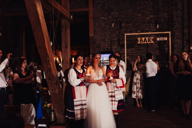 nevesta v bielych šatách, tradičný ľudový odev, sviečky v rukách, tehlový bar interiér, nočná slávnosť, hostia v tme. Karolinenhof Farm, Hainburg.
