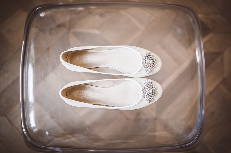 detail svadobných lodičiek s brošňami v priehľadnej krabici na parketovej podlahe. Art Hotel Kaštieľ Tomášov.