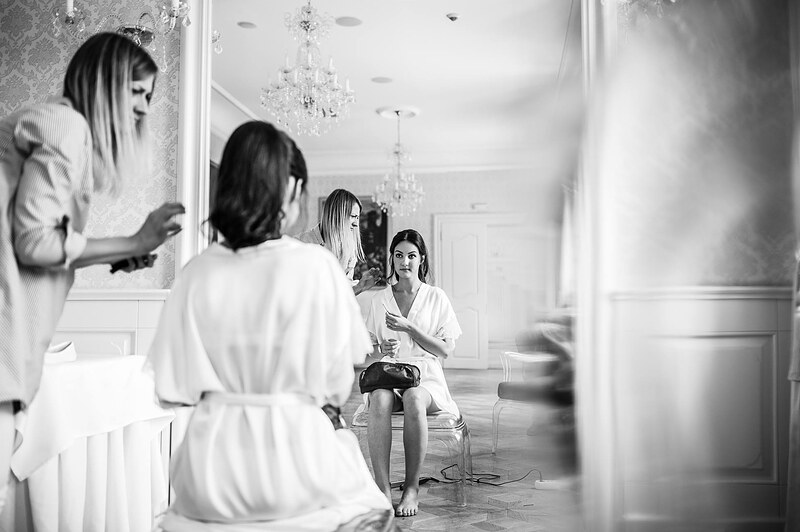 čiernobiely záber cez pootvorené dvere, kaderníčka fixuje účes, družičky sedia v pozadí. Art Hotel Kaštieľ Tomášov.