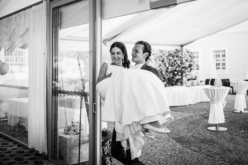 čiernobiely záber, ženích nesie nevestu v náručí do svadobného stanu. Art Hotel Kaštieľ Tomášov.