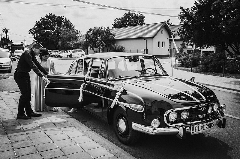 muž otvára dvere auta, nevesta vstupuje do vozidla, čiernobiely snímok, parkovisko pred domom, svadobné auto, deň svadby. Kaštieľ Villa Bork, Borčice.