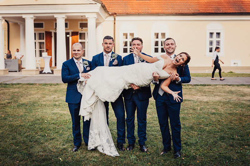 nevesta v bielych šatách, ženích a svedkovia, smiech a radosť, klasická budova v pozadí, deň svadby, skupina mužov v modrých oblekoch. Kaštieľ Villa Bork, Borčice.