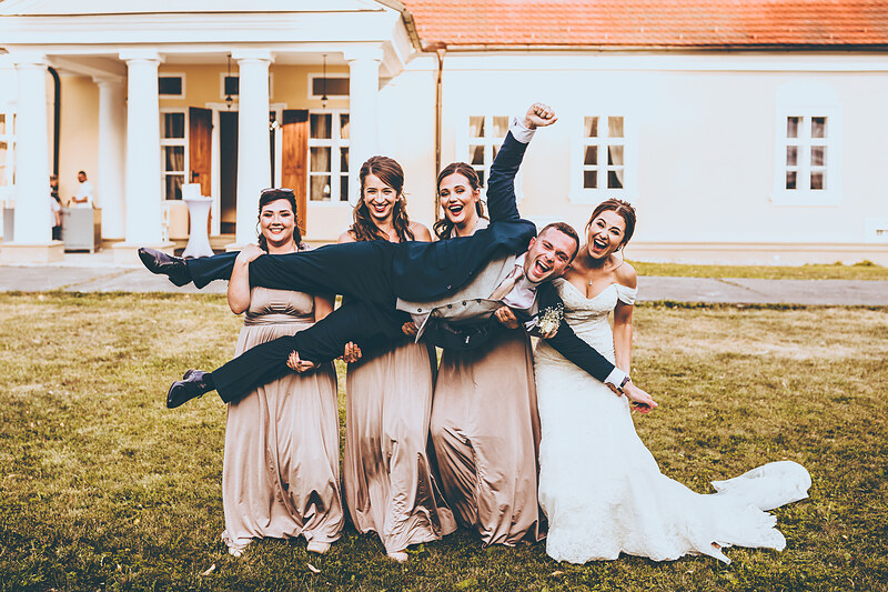 nevesta v bielych šatách, ženích v čiernom obleku, svadobná párty na trávniku, slnečný deň, radosť a smiech, klasická biela vila v pozadí. Kaštieľ Villa Bork, Borčice.