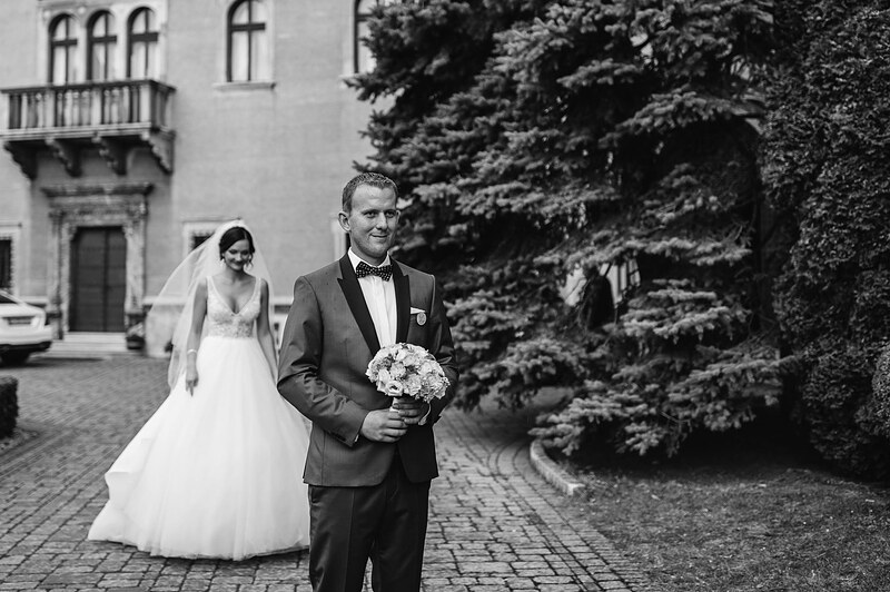 novomanželia pred historickou budovou, ženích v sivom smokingu, nevesta s kyticou bielych ruží, tvarované tuje. Hotel Jeleň, Hlohovec.