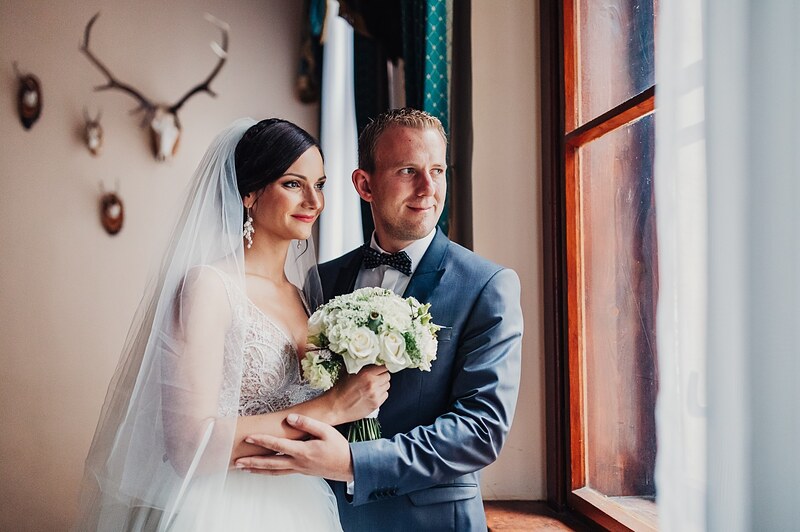 novomanželia pri okne, ženích v modrom obleku a motýliku, nevesta s kyticou, trofeje na stene. Hotel Jeleň, Hlohovec.