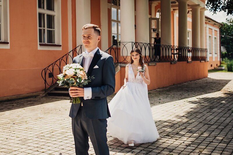 nevesta prichádza k ženíchovi pred fasádou kaštieľa s arkádami, ženích drží kyticu. Kaštieľ Klobušice.
