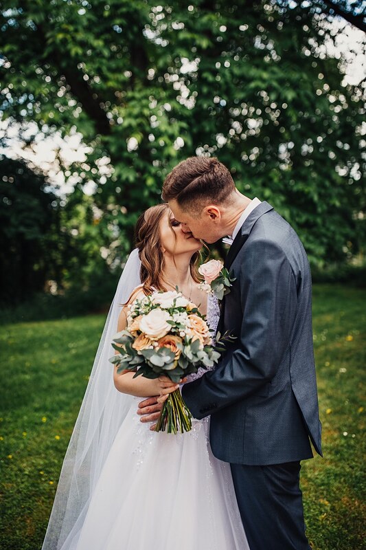 novomanželia sa bozkávajú na trávniku, nevesta drží kyticu marhuľových ruží. Kaštieľ Klobušice.