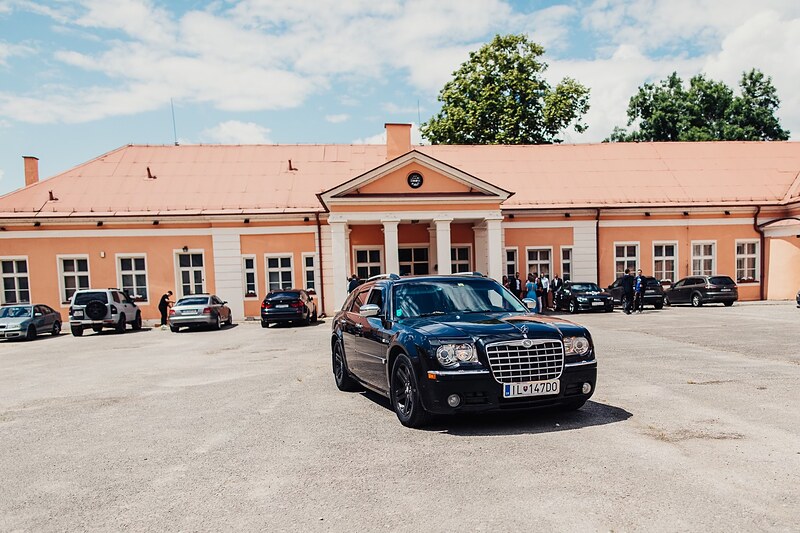 svadobné auto zaparkované pred kaštieľom, oranžová fasáda a modrá obloha s oblakmi. Kaštieľ Klobušice.