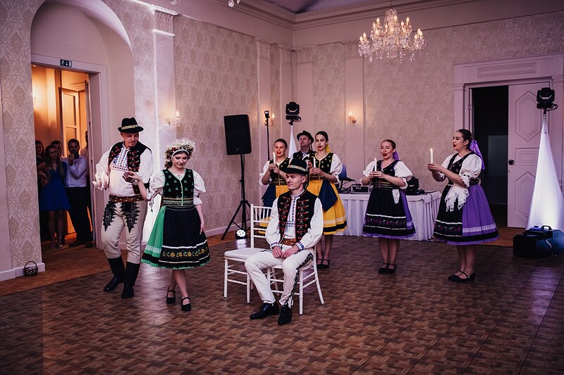 folklórny súbor vo fialovo-žltých krojoch prichádza do sály, ženích sedí na stoličke v strede. Kaštieľ Klobušice.