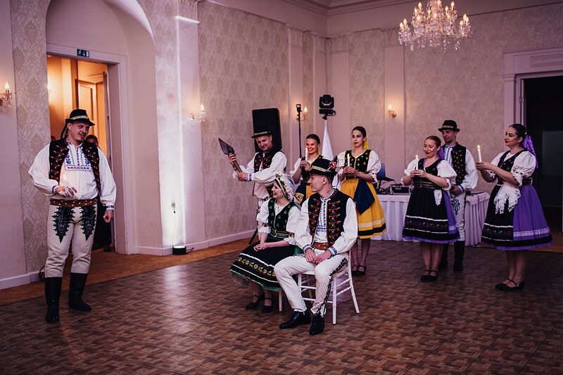 tanečníci v krojoch so sviečkami okolo sediaceho ženícha, čepčenie v kaštieľskej sále. Kaštieľ Klobušice.