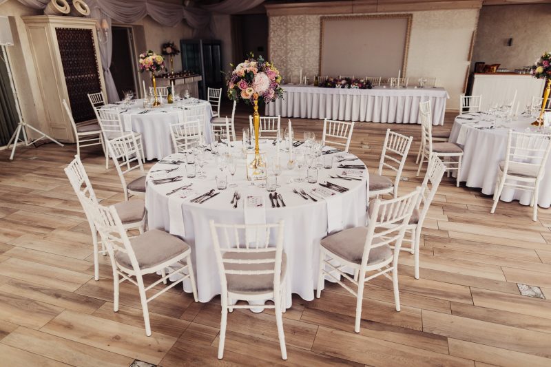 okrúhly stôl s kvetmi, biele stoličky s vankúšmi, pripravená svadobná sála, zlaté vázy s ružami, elegantný banketový priestor, dekorácie na hlavnom stole. Hotel Zlatý Kľúčik, Nitra.