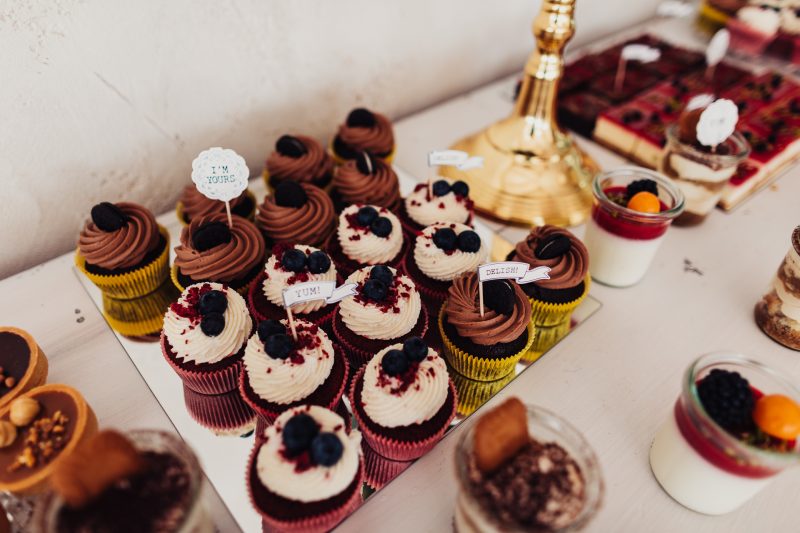 cupcakes na stole, čokoládové a vanilkové zákusky, čierne bobule na dezerte, sladký stôl na svadbe, zlatý dekor v pozadí, denné svetlo v interiéri. Hotel Zlatý Kľúčik, Nitra.