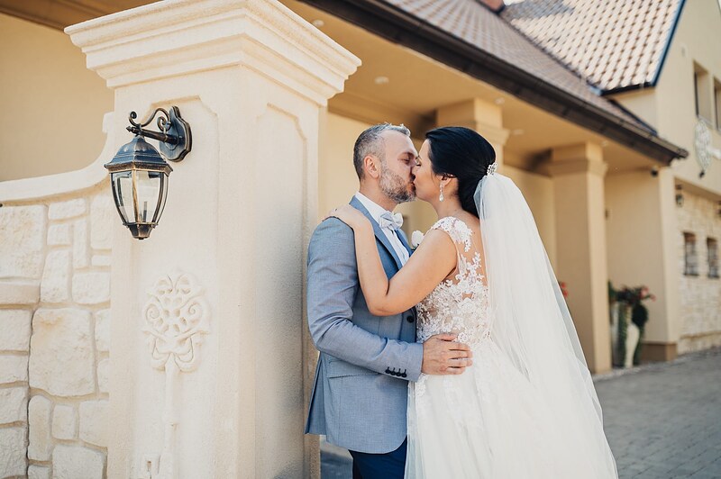 pár sa bozkáva pri kamennej stene s lampášom, ženích v svetlomodrom obleku, nevesta so závojom. Hotel Zlatý Kľúčik, Nitra.