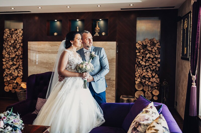 novomanželia v hotelovej hale, stena s naukladaným drevom, fialová pohovka, nevesta s kyticou. Hotel Zlatý Kľúčik, Nitra.