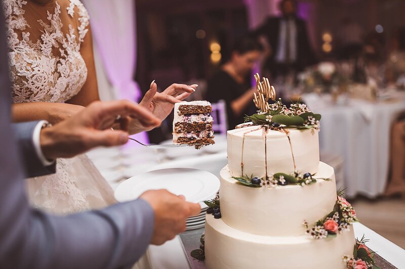 krájanie torty, trojposchodová biela torta s kvetmi, ruky podávajú tanierik s kúskom. Hotel Zlatý Kľúčik, Nitra.