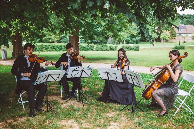 sláčikové kvarteto hrá v parku, husle, viola a violončelo, notové stojany na tráve. Kaštieľ Orlové, Považská Bystrica.
