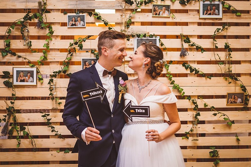 novomanželia pri fotokútiku z drevených paliet, tabuľky Mr a Mrs v rukách, brečtan a rámiky s fotkami. Penati Golf Resort, Senica.