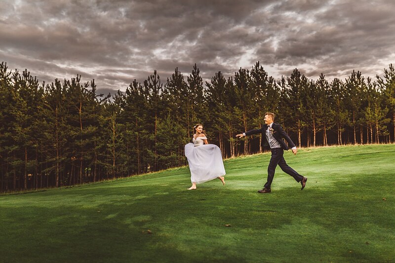 nevesta uteká bosá po zelenom fairwayi, ženích za ňou, tmavé búrkové oblaky nad borovicami. Penati Golf Resort, Senica.