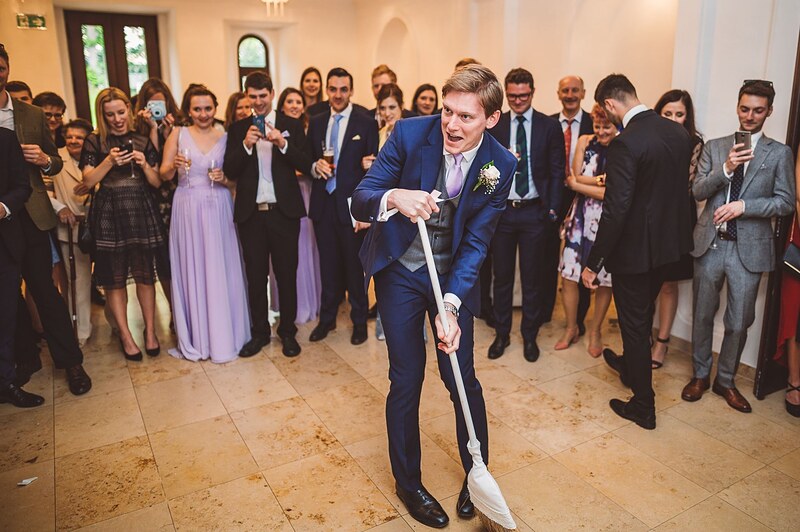 ženích zametá črepy metlou, hostia v kruhu okolo neho fotia mobilmi. Chateau Appony, Oponice.