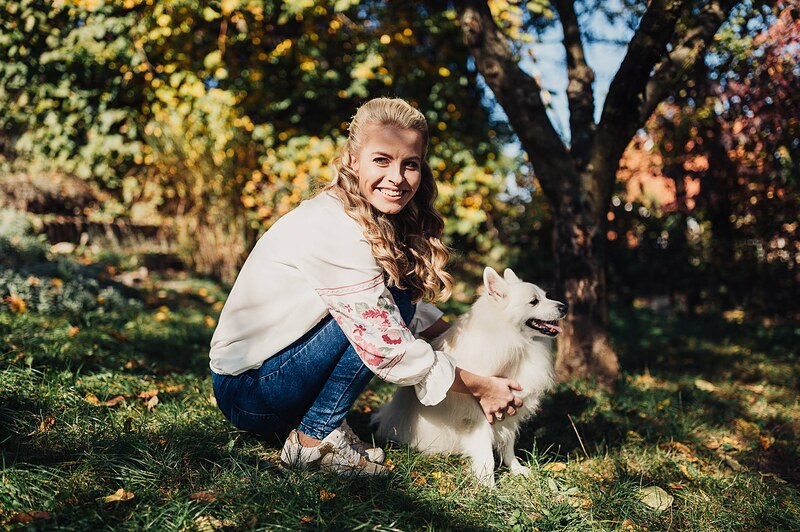 žena vo vyšívanej blúzke kľačí pri bielom psovi, jesenná záhrada, slnko v korunách stromov, ráno pred svadbou. Fatima, Trenčín.