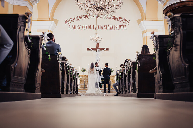 nevesta v kostole, ženích a nevesta pred krížom, svadobný obrad v chráme, svetlo zo stropu, hostia v laviciach, slávnostná atmosféra v kostole. Fatima, Trenčín.