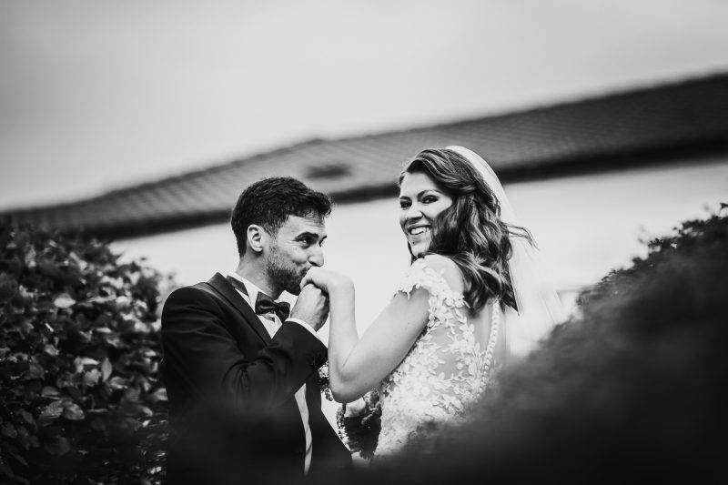 nevesta v čipke sa smeje, ženích v obleku a motýliku, pár pri rieke, most v pozadí, slnečný deň, radosť a nežnosť. Fatima, Trenčín.