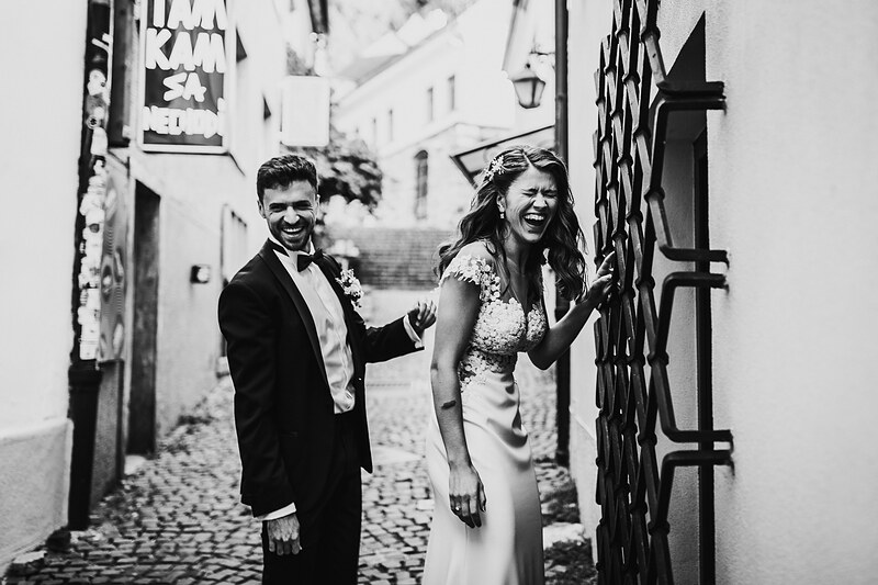 nevesta a ženích v uličke, svadobný pár sa smeje, kamenná ulička, svadobné šaty s čipkou, ženích v obleku s motýlikom. Fatima, Trenčín.