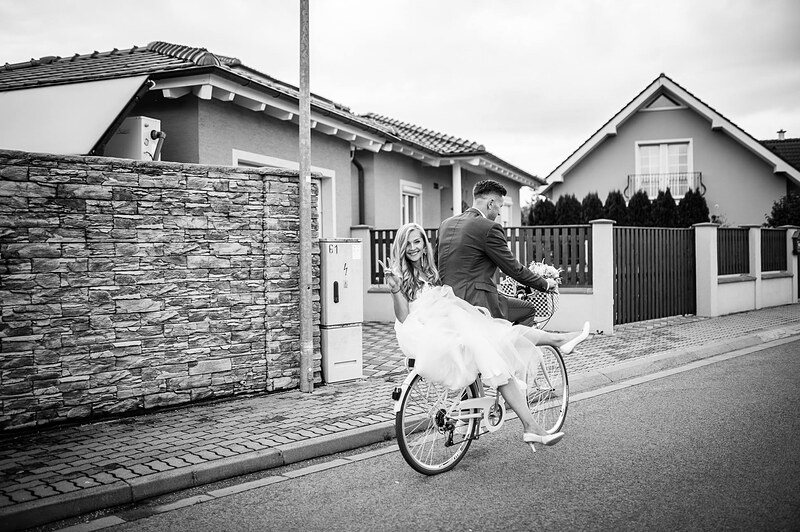 čiernobiely záber, nevesta bicykluje po ulici v tylovej sukni, ženích za ňou. Gazdovský dvor, Trenčianska Turná.