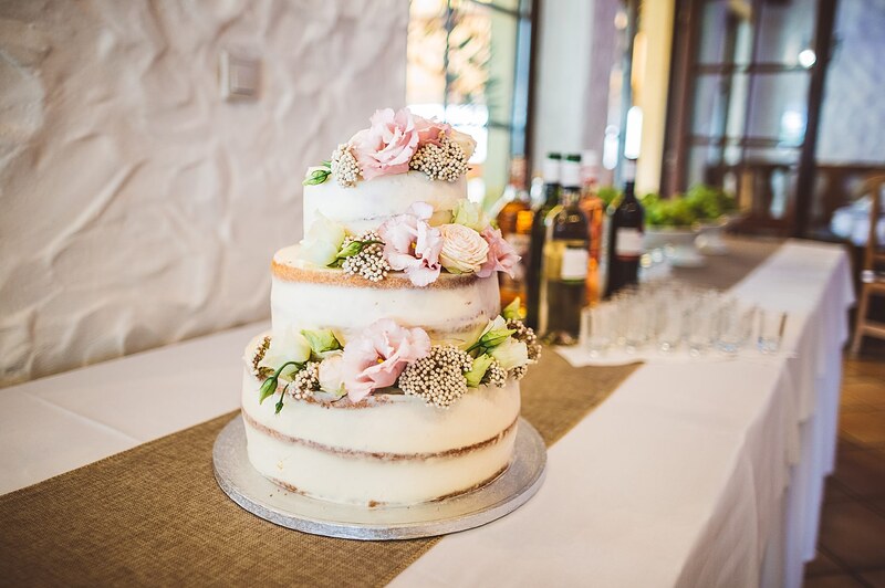 trojposchodová naked cake s ružovými kvetmi na jutovom behúni, fľaše vína v pozadí. Gazdovský dvor, Trenčianska Turná.