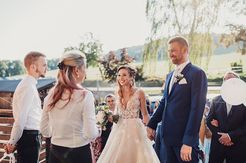 gratulácie vonku pred budovou, hostia podávajú ruky novomanželom, vŕba a kopce v pozadí. Gazdovstvo Uhliská.