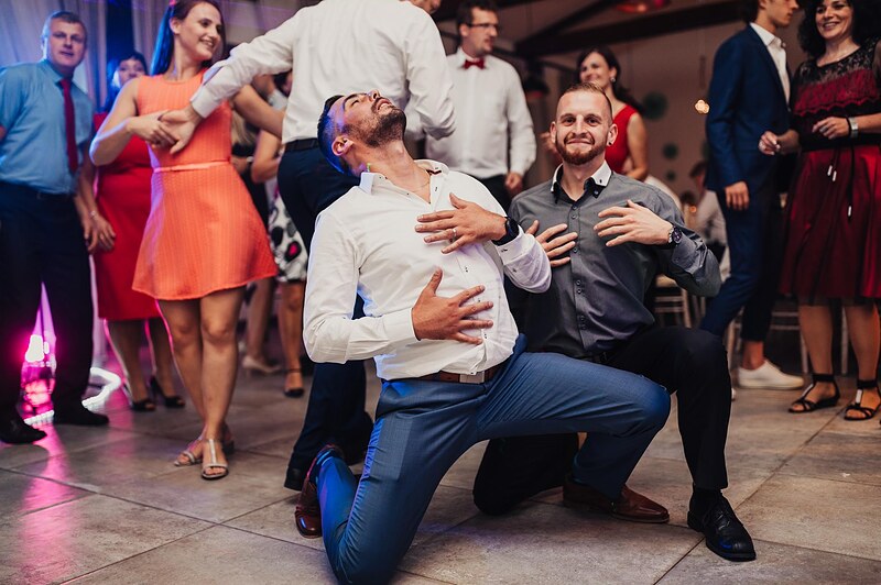 dvaja muži v košeliach predvádzajú tanečnú figúru, hostia okolo sa smejú. Gazdovstvo Uhliská.