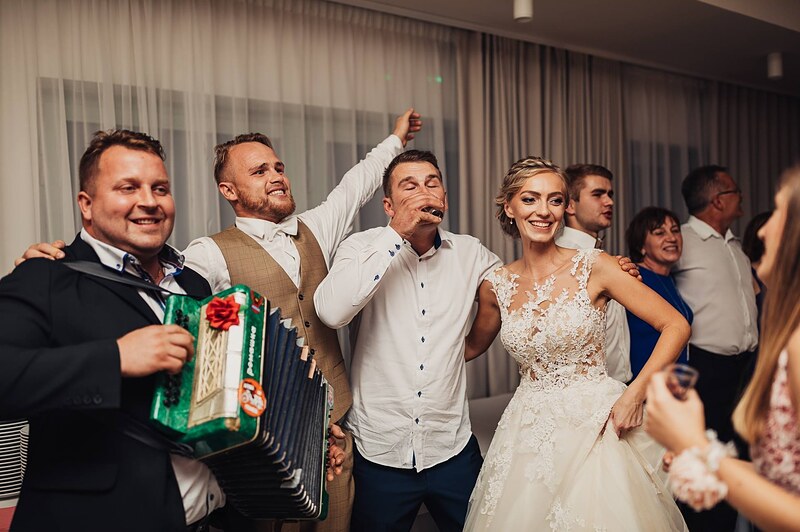 harmonikár so zelenou harmonikou spieva s hosťami, nevesta medzi nimi, veselá chvíľa v sále. Hotel Veverica, Trenčín.