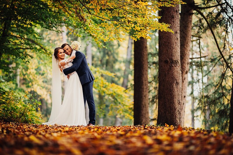 ženích objíma nevestu uprostred lesa, koberec z hnedého lístia, vysoké smreky. Hotel Veverica, Trenčín.