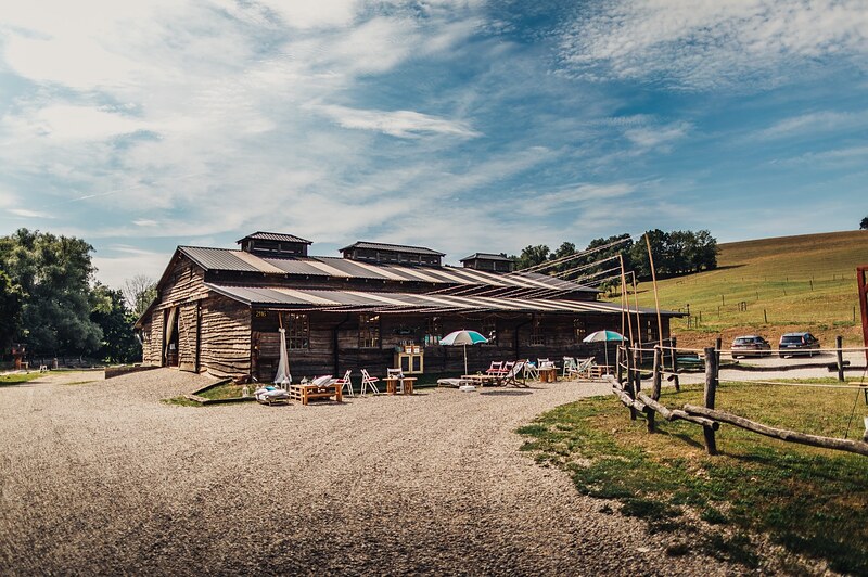 pohľad na areál ranča, dlhá drevená stodola so šindľovou strechou, ohrada a kopce v pozadí. Ranch 13, Nemšová.