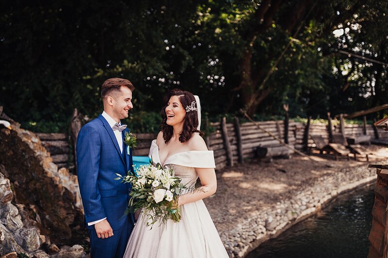 novomanželia sa na seba smejú pri jazierku, ženích v modrom obleku, kytica bielych kvetov. Ranch 13, Nemšová.