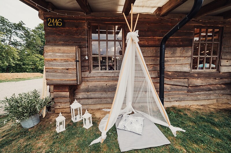detský kútik s bielym teepee pri drevenej zrubovej stene, lampáše a vankúše na deke. Ranch 13, Nemšová.