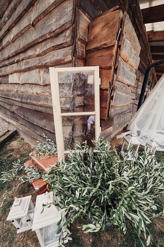 dekorácia pri zrube, staré okno opreté o stenu, olivovník a lampáše na tráve. Ranch 13, Nemšová.