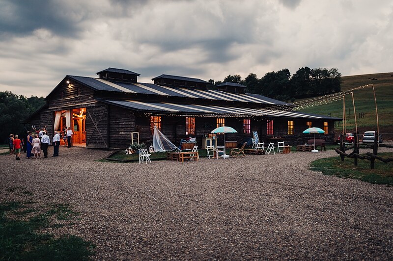 drevená stodola za súmraku, rozsvietené okná a svetelné reťaze, hostia pred vchodom. Ranch 13, Nemšová.