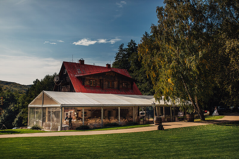 celkový pohľad na rezort, drevenica s červenou strechou a presklený párty stan, kopce Bielych Karpát v pozadí. Vila Sokolka, Trenčín.