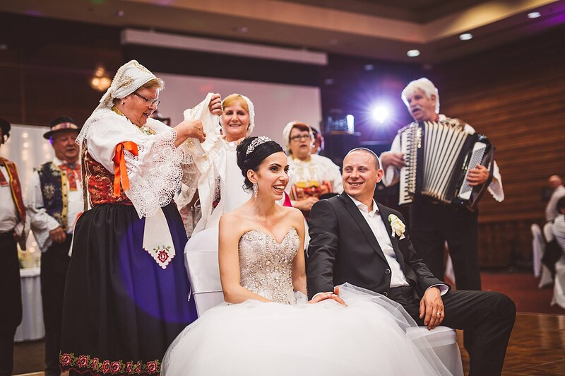 žena v kroji nasadzuje neveste čepiec, ženích sedí vedľa, súbor a harmonikár v pozadí. Holiday Inn Trnava.