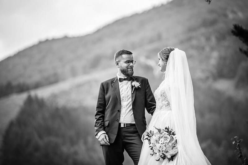 čiernobiely portrét novomanželov na lúke, zalesnený svah za nimi, kytica v ruke nevesty. Kaštieľ Krasňany, Žilina.