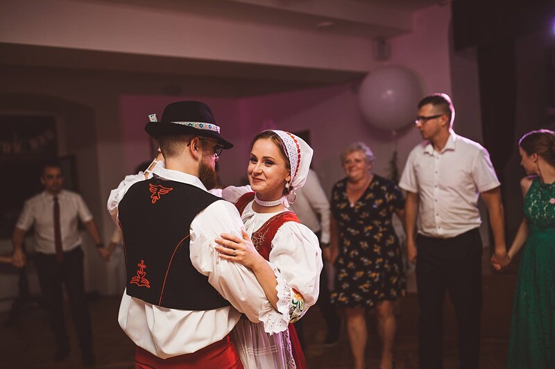 nevesta v čepci tancuje s mužom v kroji a klobúku, hostia sa držia za ruky okolo nich. Kaštieľ Krasňany, Žilina.