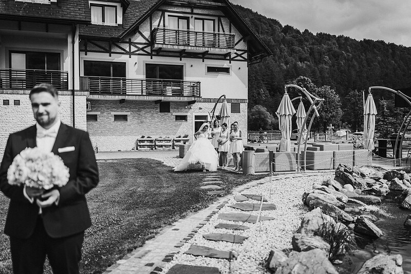 ženích s kvetmi, nevesta v bielych šatách, horský hotel v pozadí, slnečný deň v údolí, svadobný ceremoniál vonku. Village Resort Hanuliak.