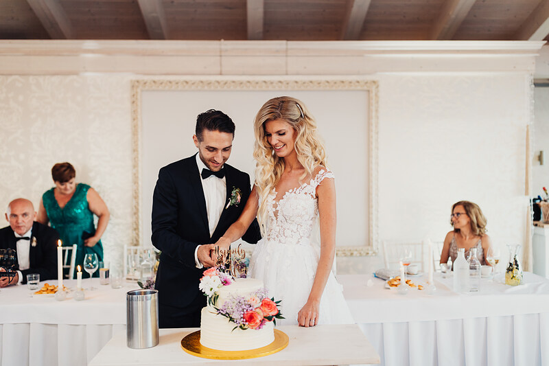 nevesta a ženích pri torte, krájanie svadobnej torty, biele interiéry s dekoráciami, svadobný banket, pár pri stole, svetlá miestnosť s hosťami. Hotel Zlatý Kľúčik, Nitra.