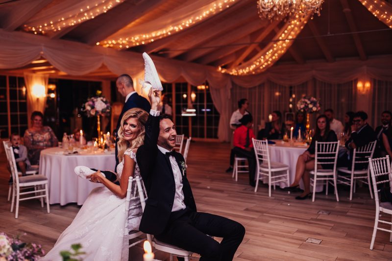 nevesta a ženích sedia, svadobná tanečná sála, teplé svetlá pod stropom, hostia pri stoloch, zlaté girlandy a drapérie, večerná slávnosť v interiéri. Hotel Zlatý Kľúčik, Nitra.